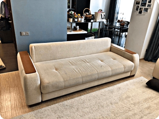Worn modern beige sofa with faded fabric and sagging seat cushions before restoration in New York