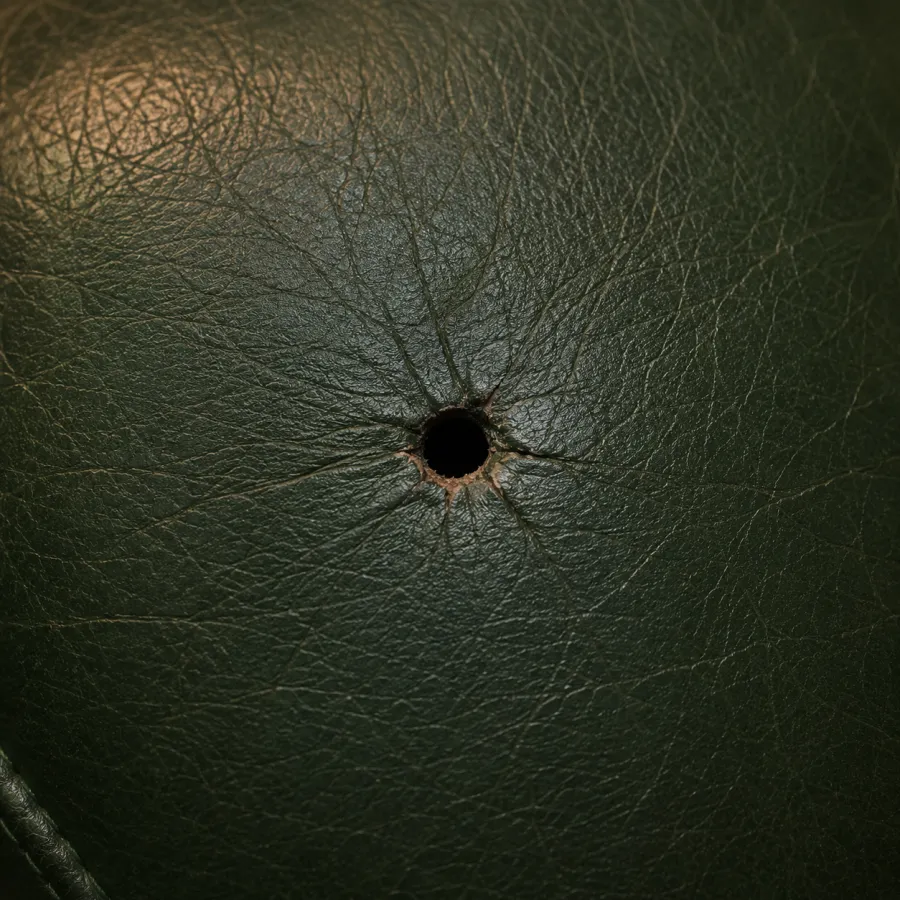 Round burn hole in dark green leather with creases radiating out from the opening