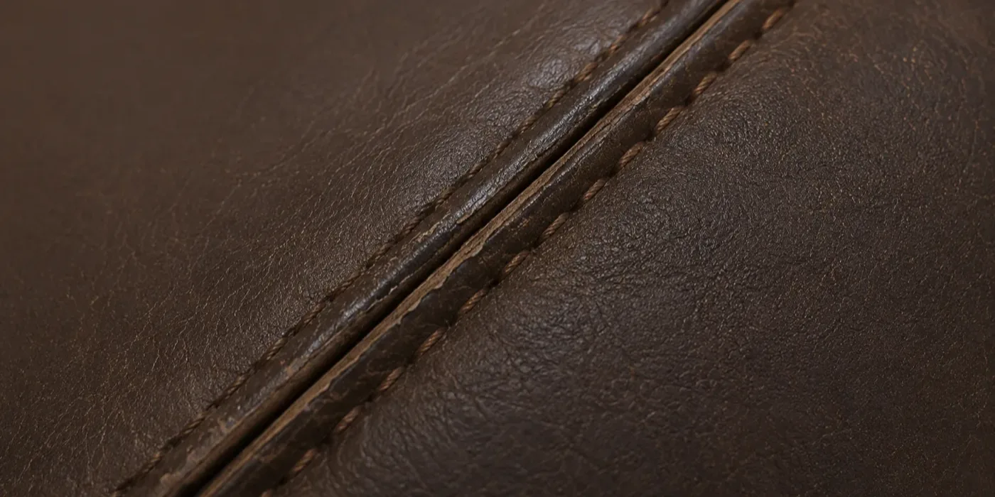 A restored seam on brown leather upholstery, closed and matched to the panel