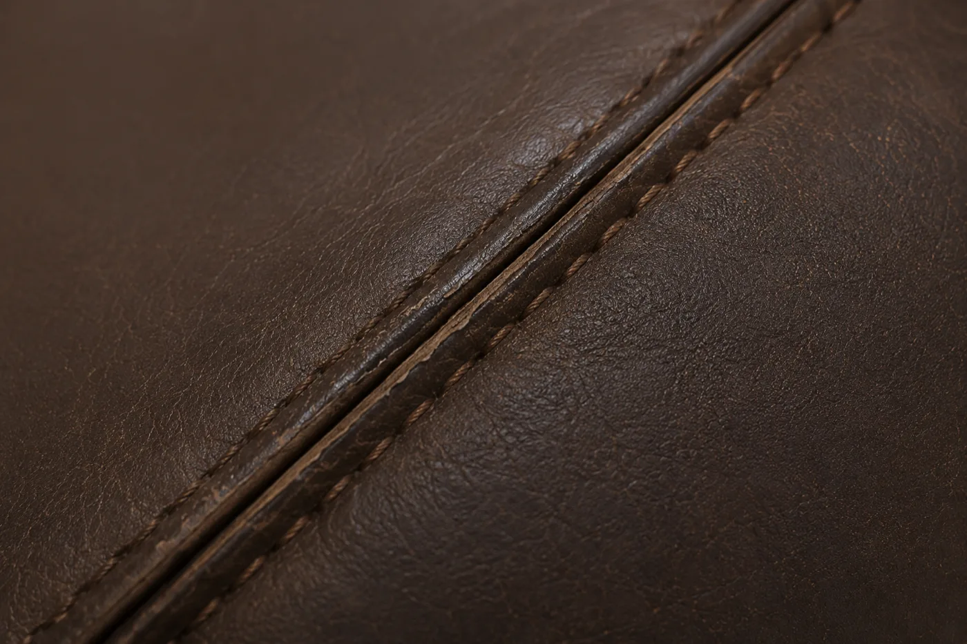 A closed and restored seam on a brown leather booth, the contrast stitching even and the colour continuous