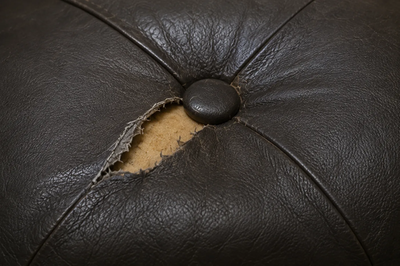 Tear in black booth leather beside a tufting button