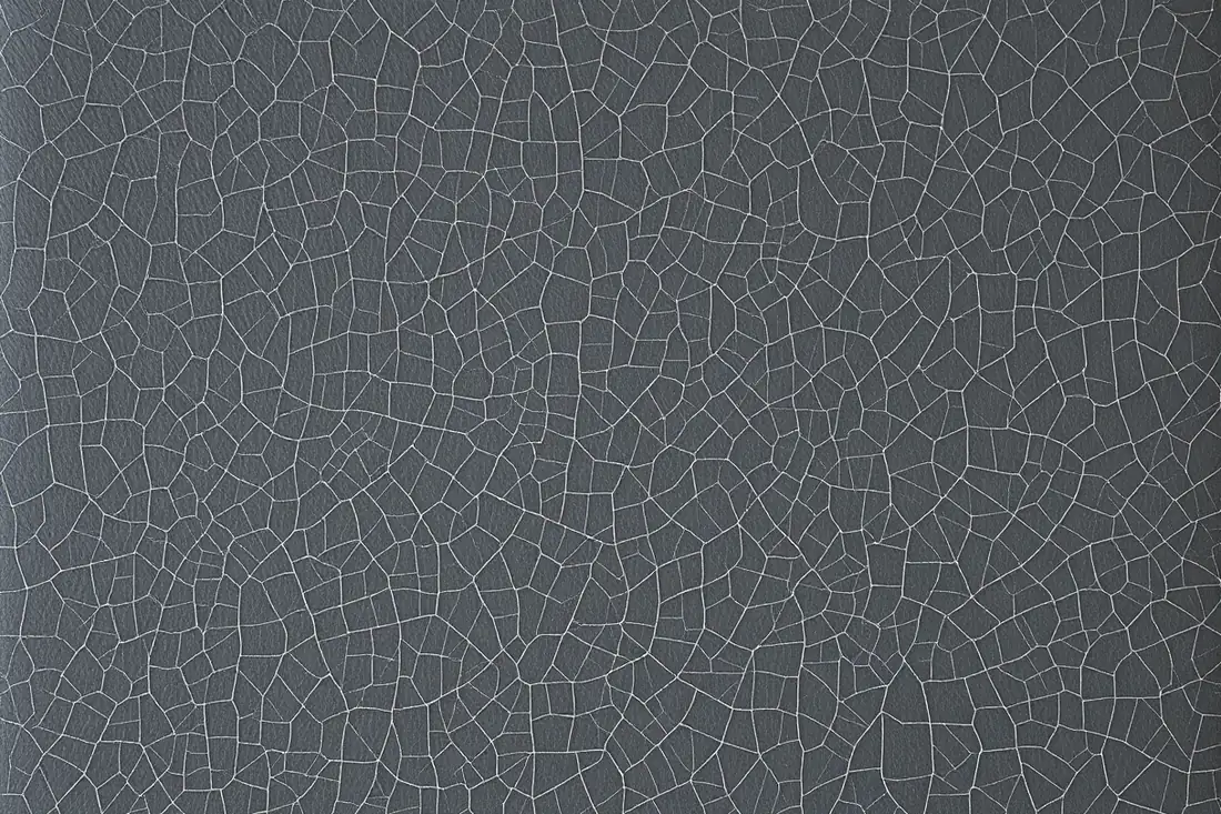 Fine hairline crazing covering an entire dark vinyl chair back, the surface dulled and chalky