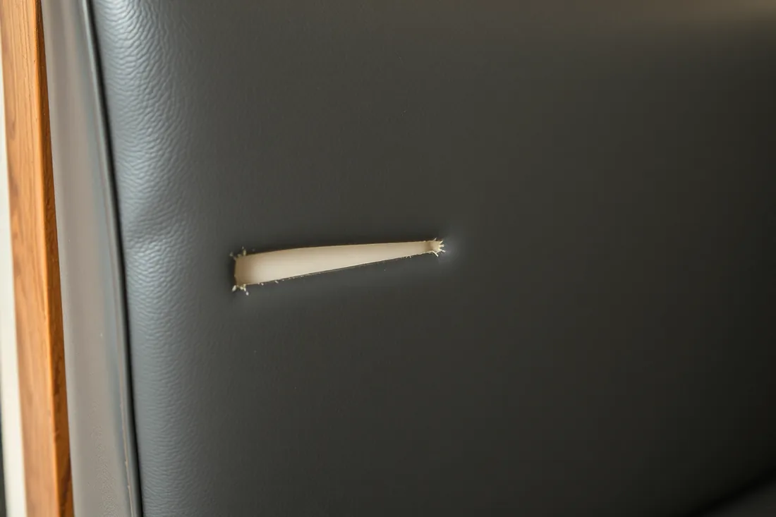 A single clean cut through a dark vinyl booth seat, the vinyl around it smooth and undamaged