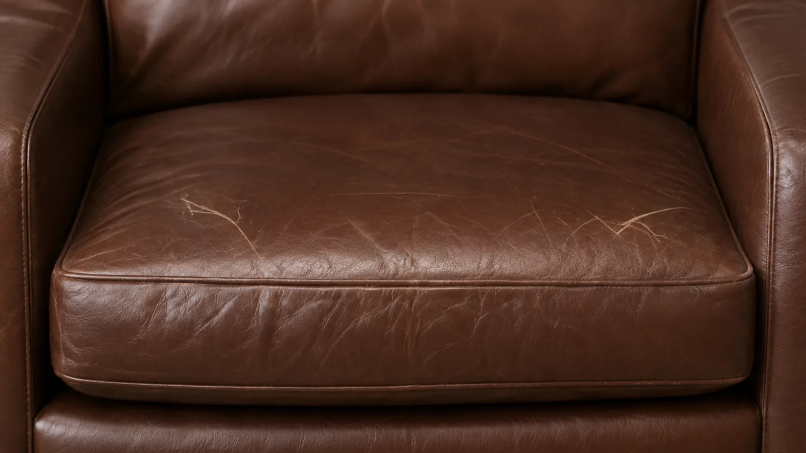 A used corrected grain leather seat cushion showing mild sheen change and light creasing