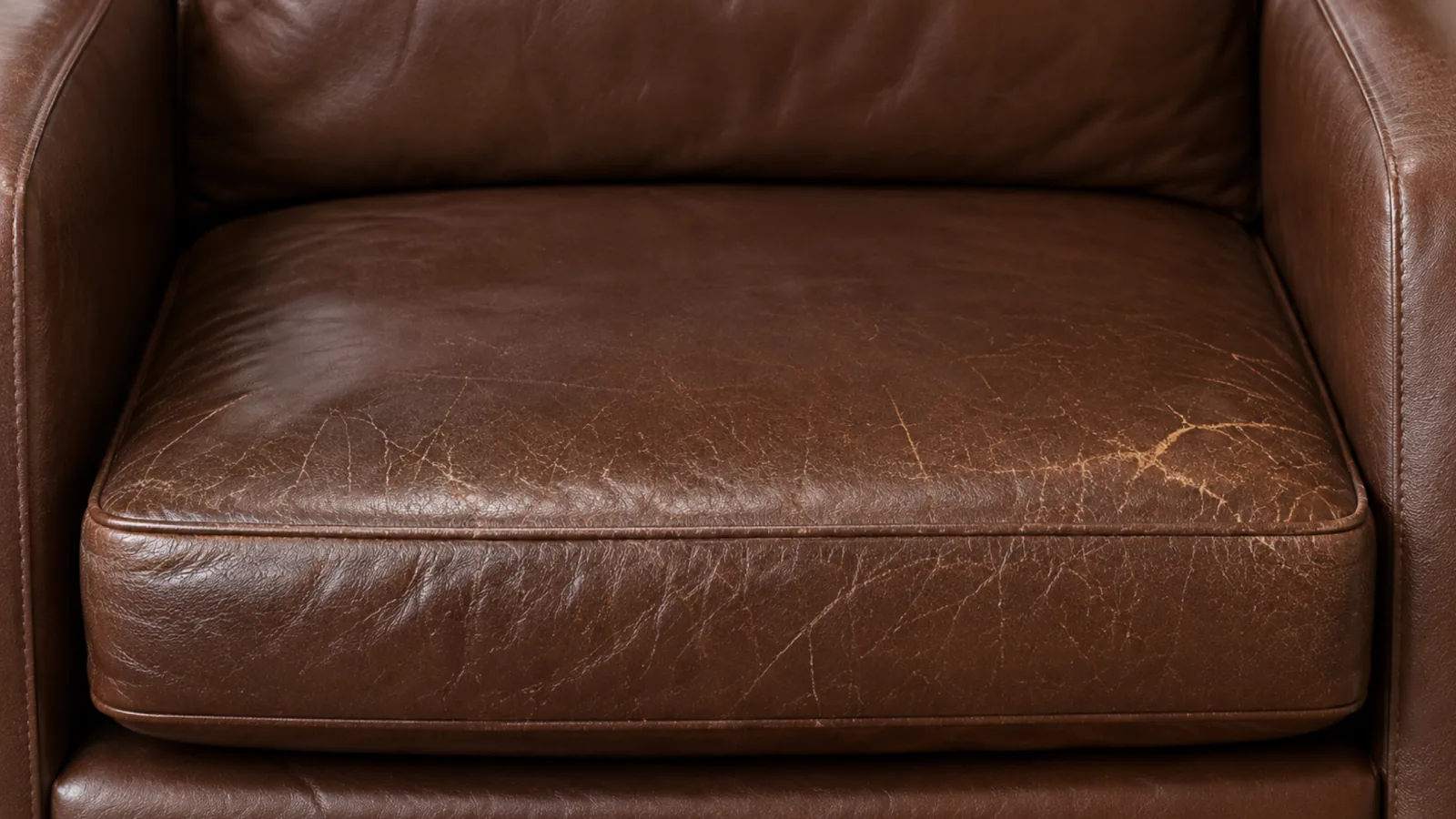 A worn corrected grain leather seat cushion with pigment loss and scratching across the front