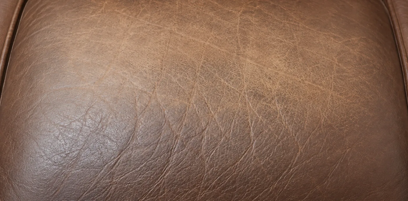 A brown corrected grain leather arm where the pigment has worn away to a lighter patch