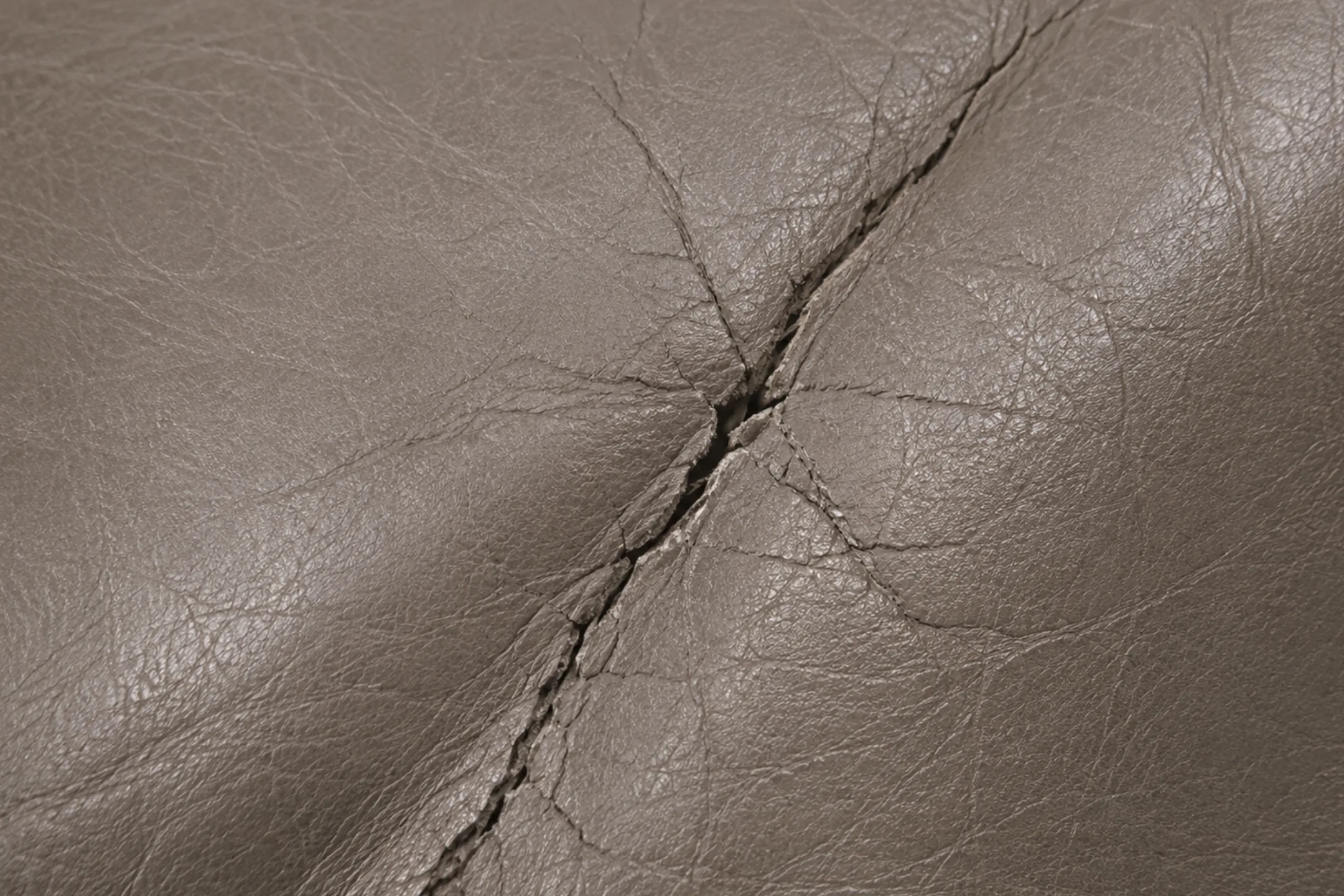 A deep crack split open along a flex line in semi-aniline leather, exposing the dry hide beneath