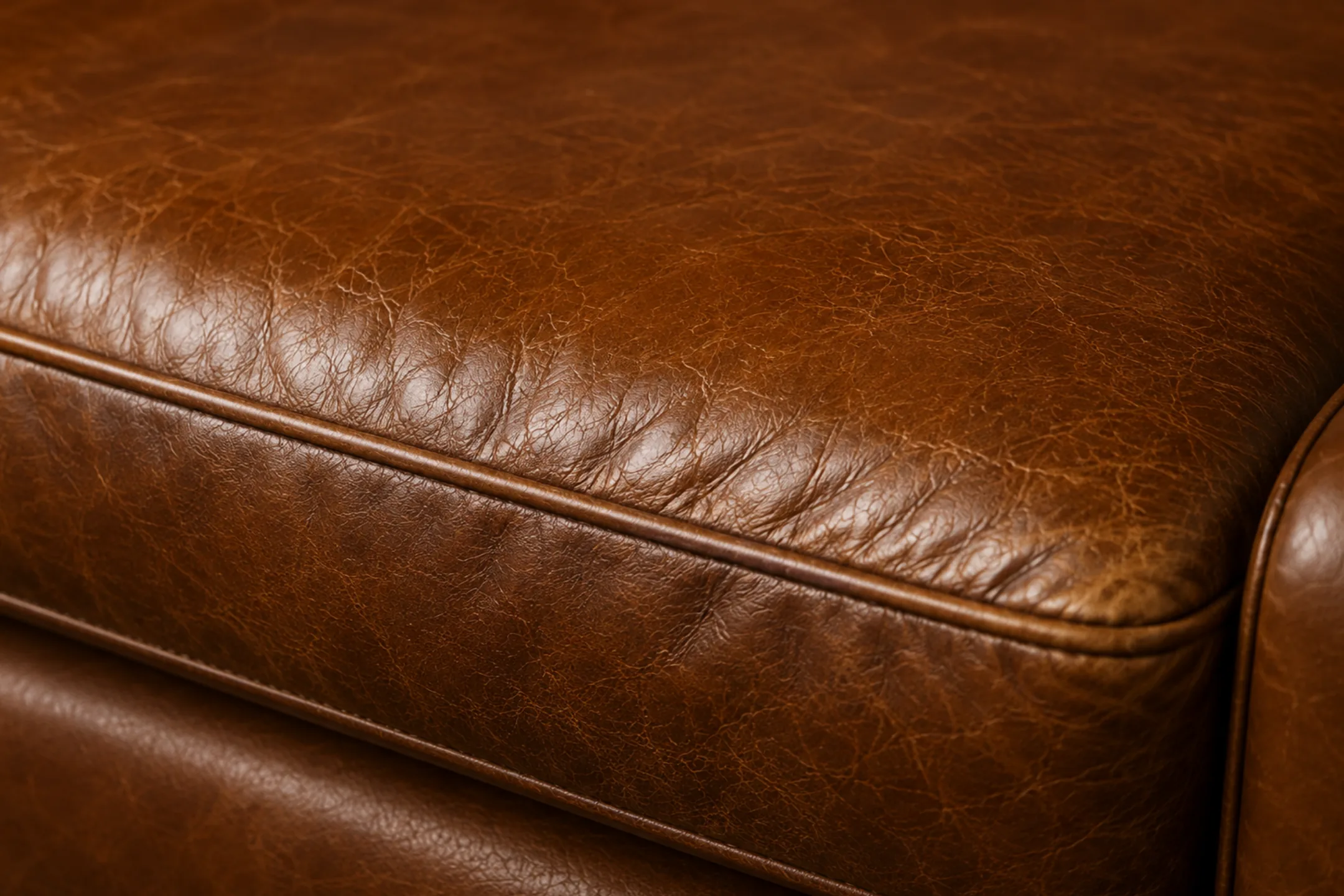 Close-up of a tan semi-aniline seat cushion front edge, the finish rubbed thin and gone hazy along the crown