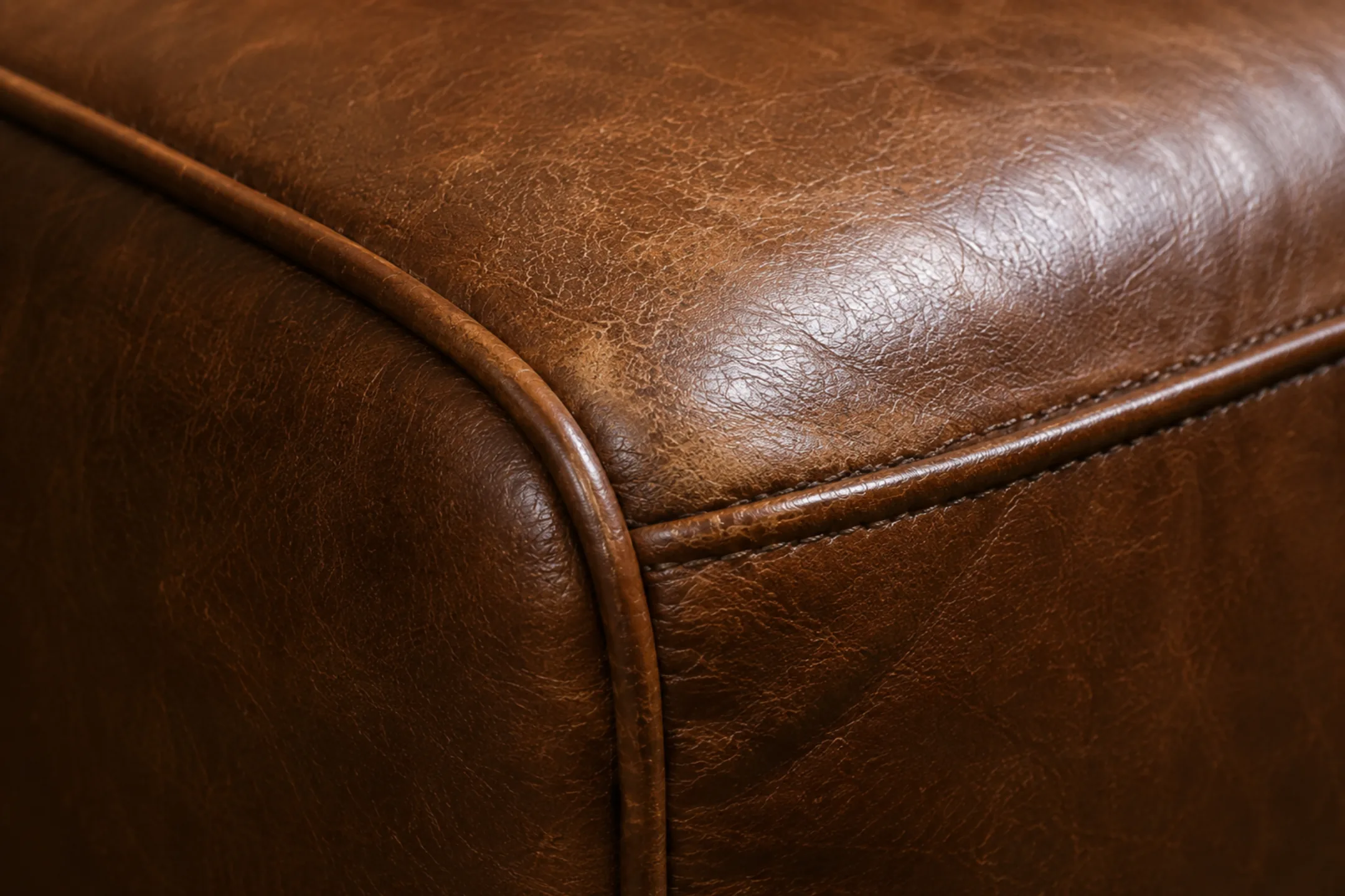 Close-up of a semi-aniline leather back cushion darkened and glossy where hair and skin oils have saturated the finish