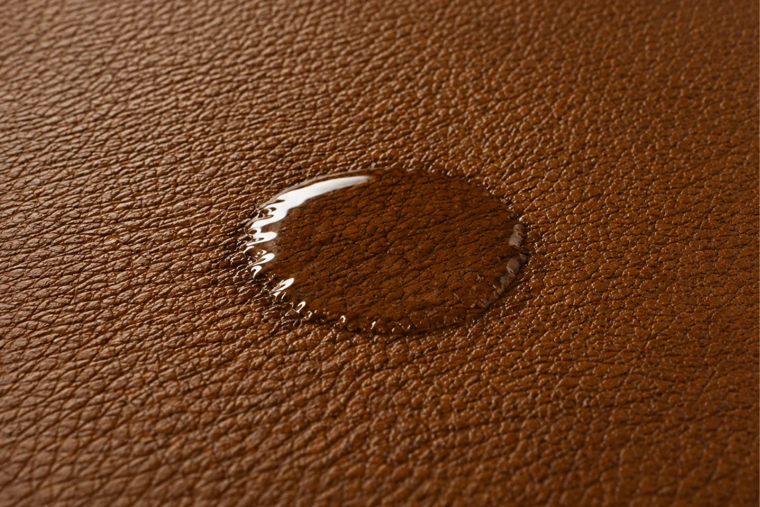 Water droplet flattened and spreading on brown leather, showing a thinning protective finish