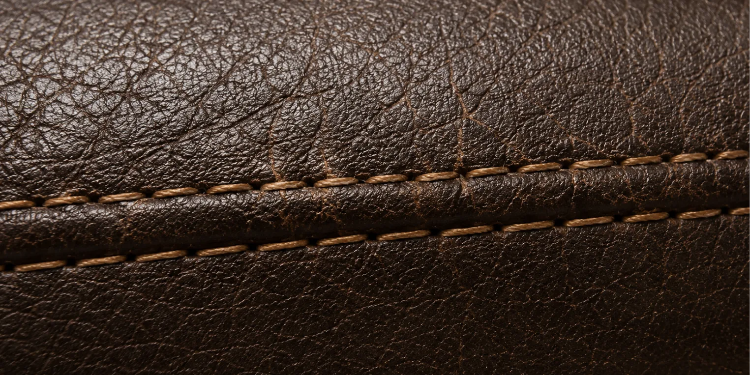 Fine cracks running parallel to a contrast-stitched seam on a brown faux leather panel