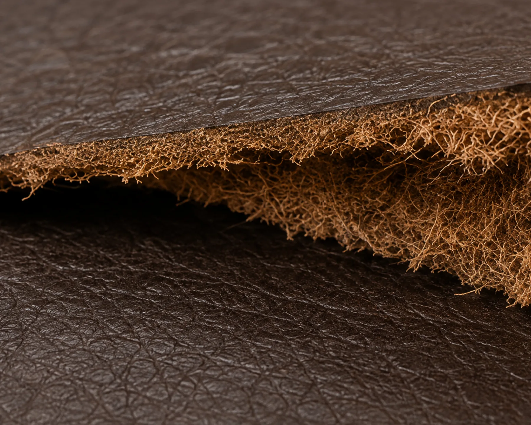 A torn faux leather edge peeled back to expose the fibrous textile backing underneath