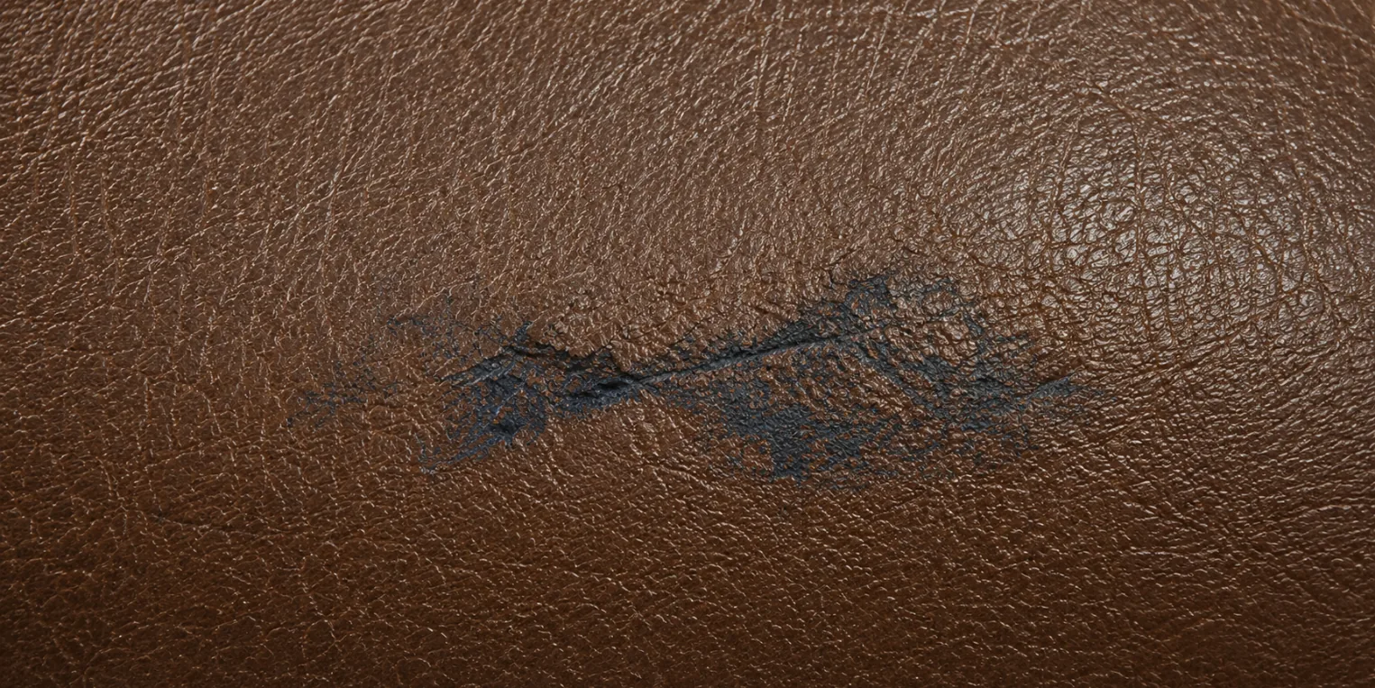 A dark blue-black dye stain sitting in the grain of a tan faux leather cushion