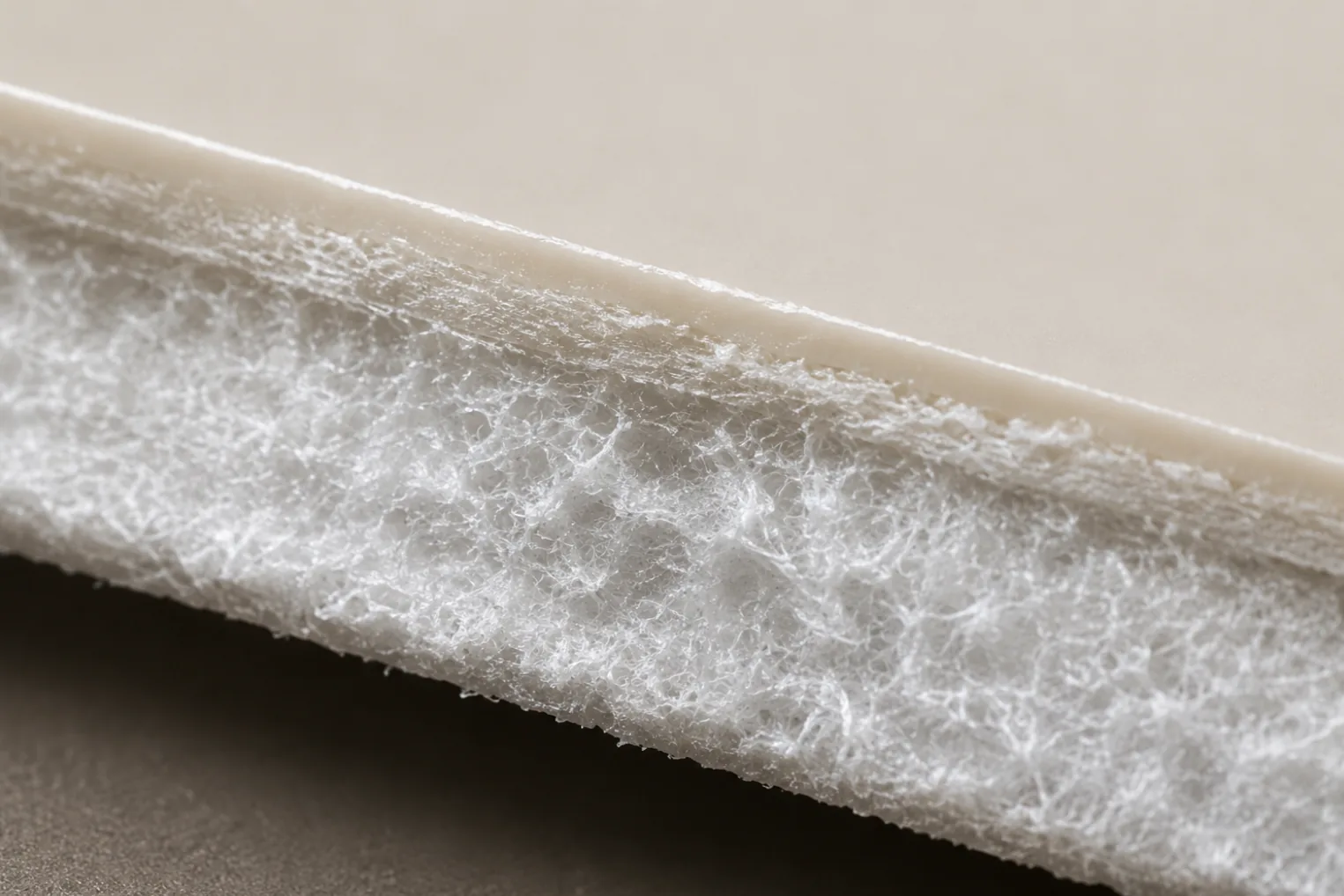 A cut edge of faux leather showing the smooth polymer film sitting on top of its fibrous backing