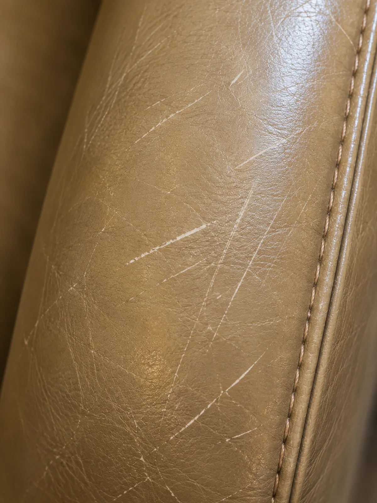 White scratch marks scored across a tan hotel leather chair arm beside the seam