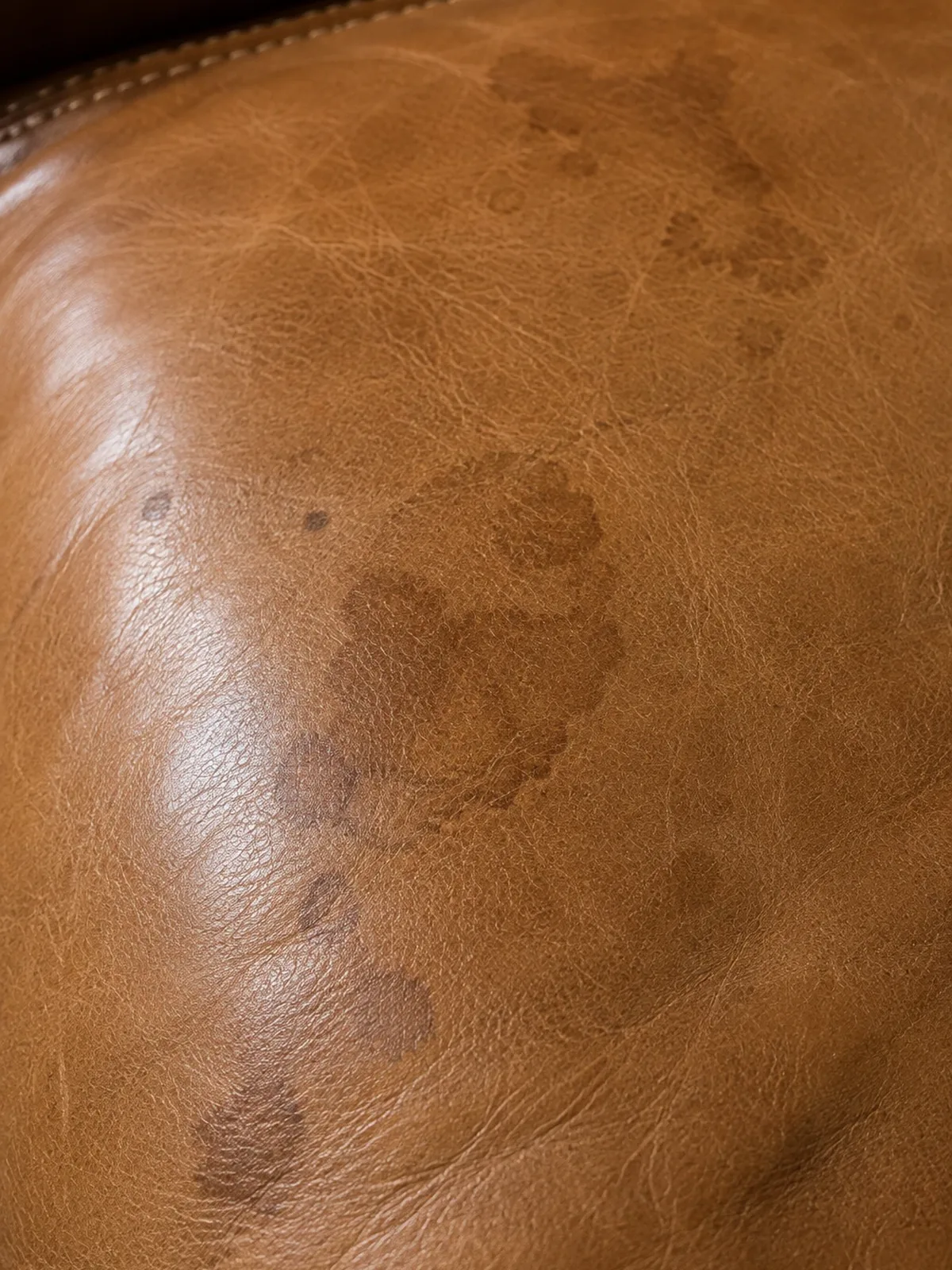 Dark blotchy staining across the seat of a brown hotel leather armchair