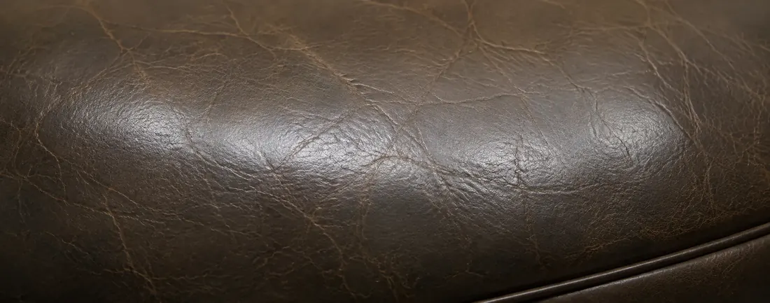 Dark leather cushion with colour rubbed off the raised grain