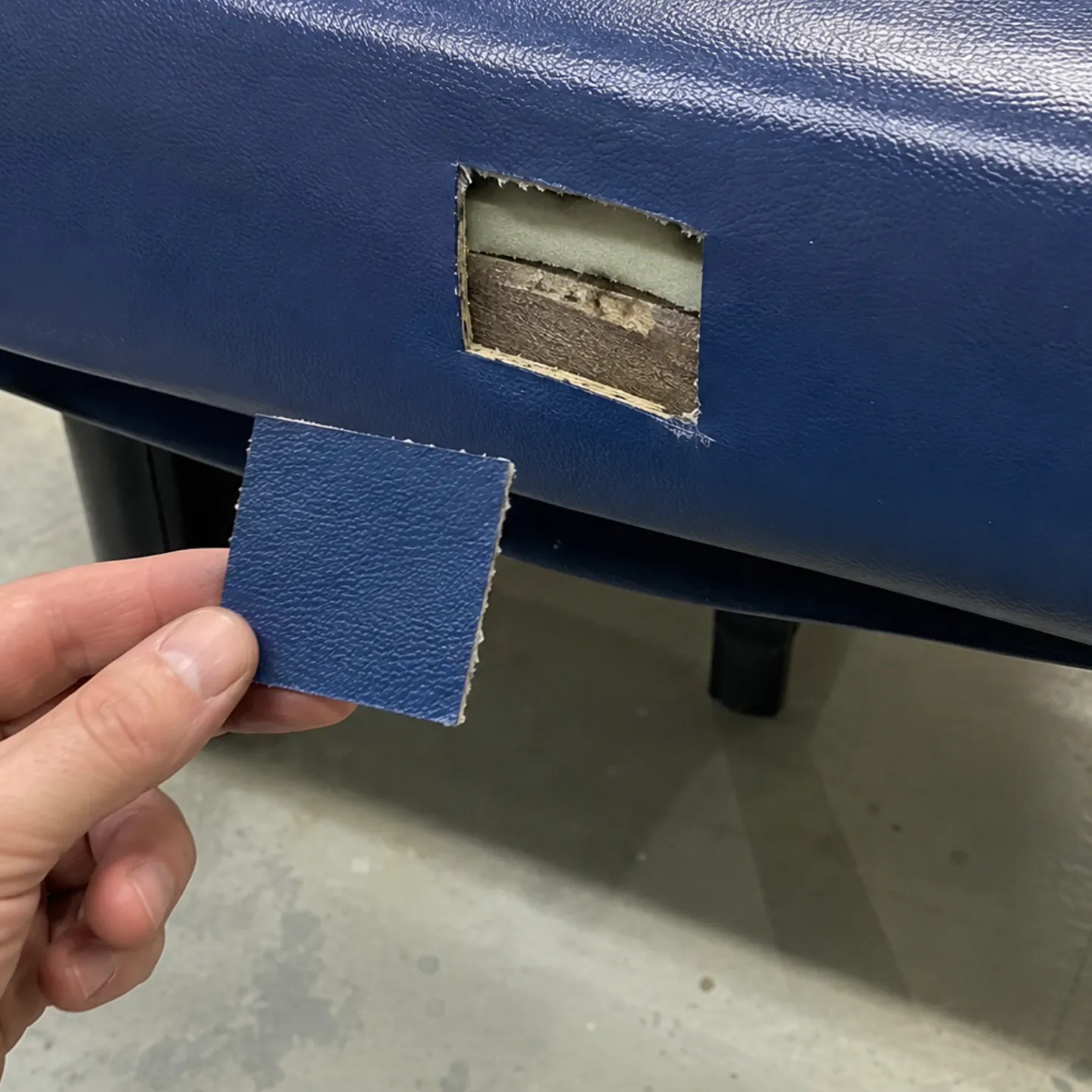 Leather material matching in progress: a cutting held against a commercial banquette to read grain, thickness and finish against the original