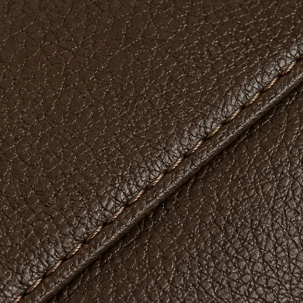 Macro of a dark brown faux leather panel with a stitched seam running across it, the printed grain slightly too regular to be a natural hide