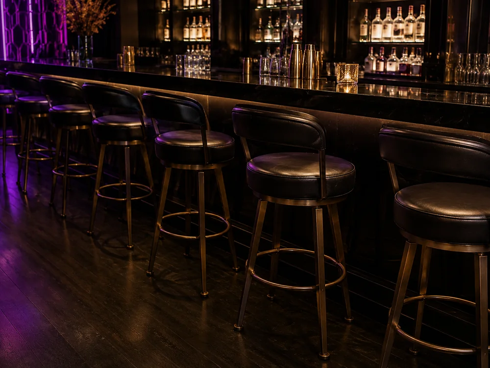Row of black leather swivel bar stools with brass frames along a nightclub bar