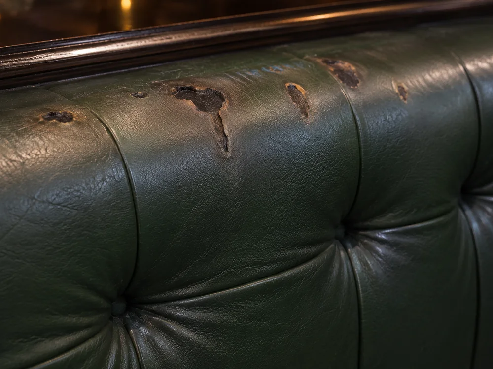 Row of burns along the buttoned back of a green leather chesterfield