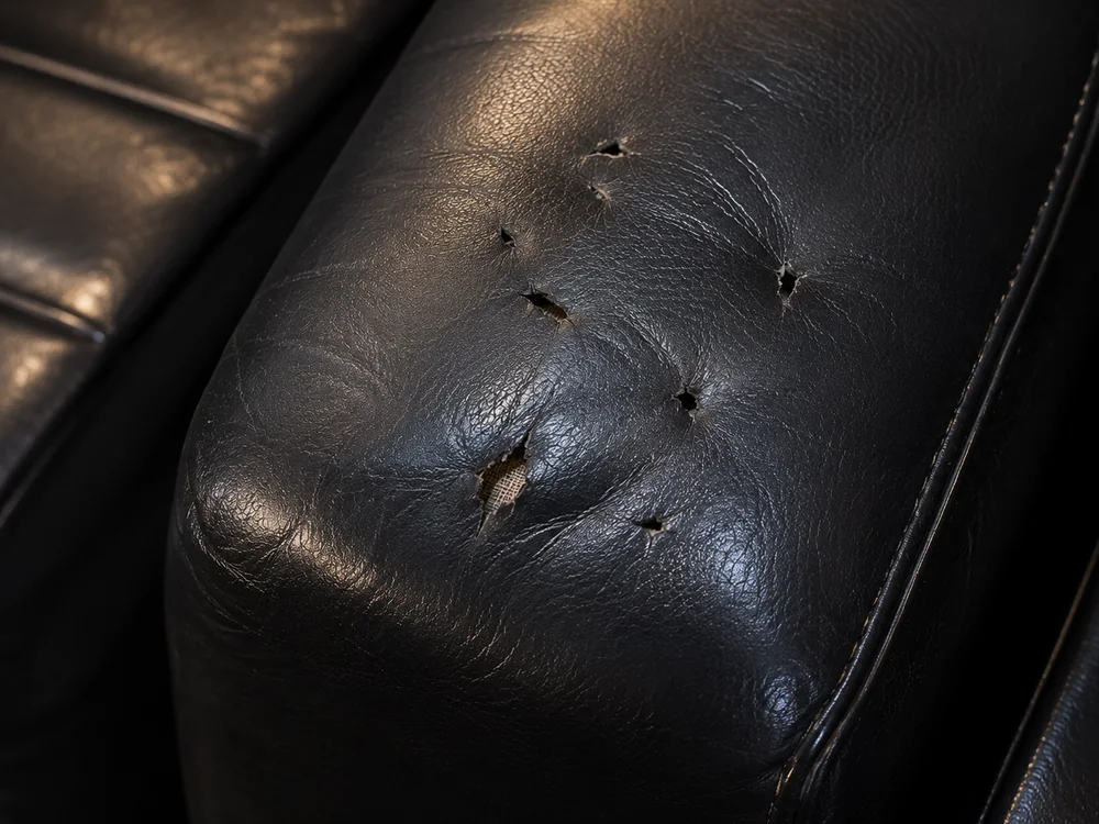 Heel punctures across the arm of a black leather club seat