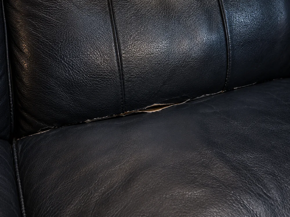 Black leather seat split open along the seam where the back meets the cushion