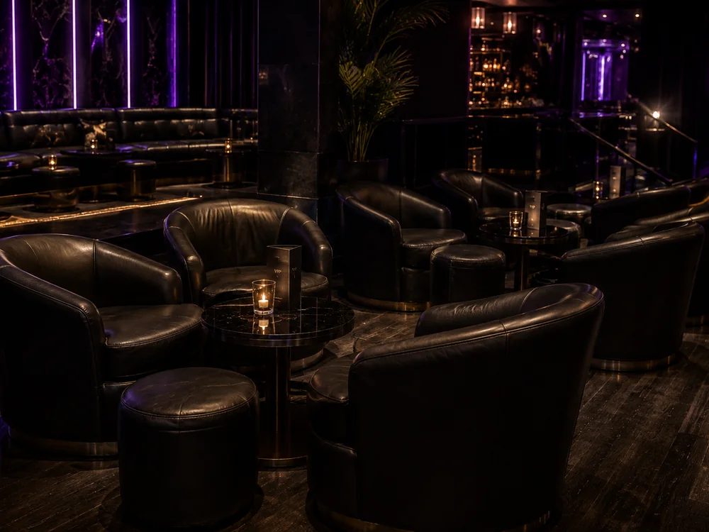 Black leather barrel club chairs and round ottomans in a nightclub lounge