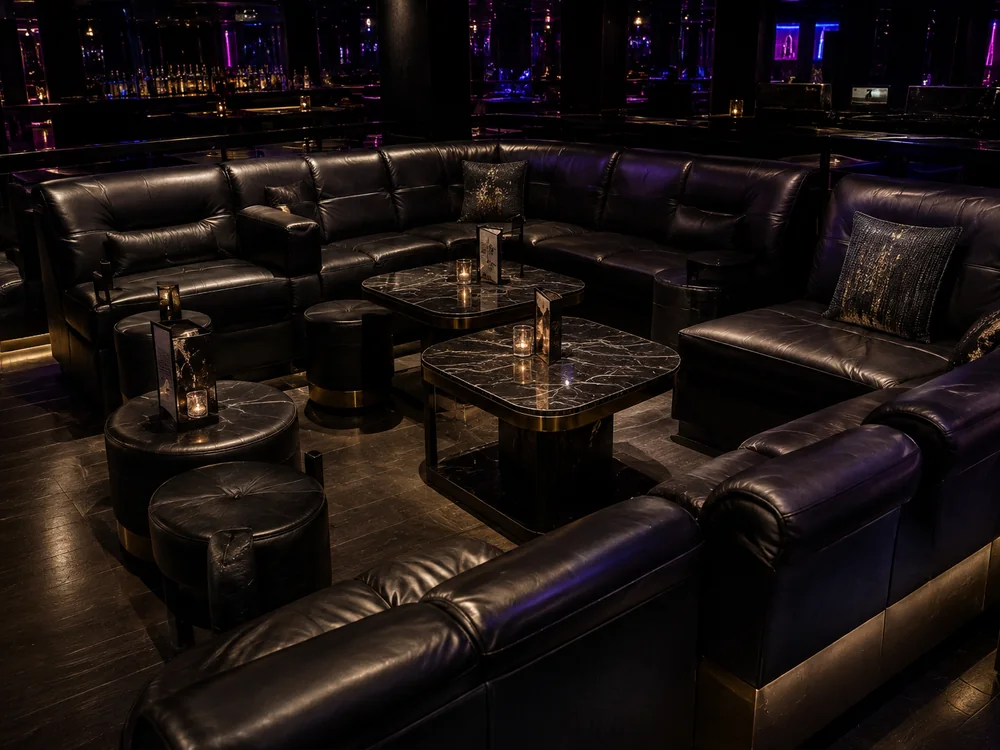 Black leather lounge sofas and ottomans around marble cocktail tables in a nightclub