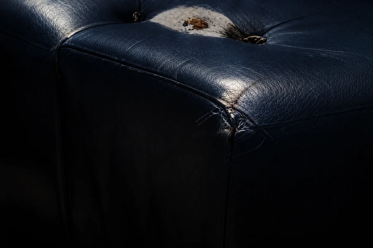 Burn hole through navy vinyl seating exposing the foam beneath