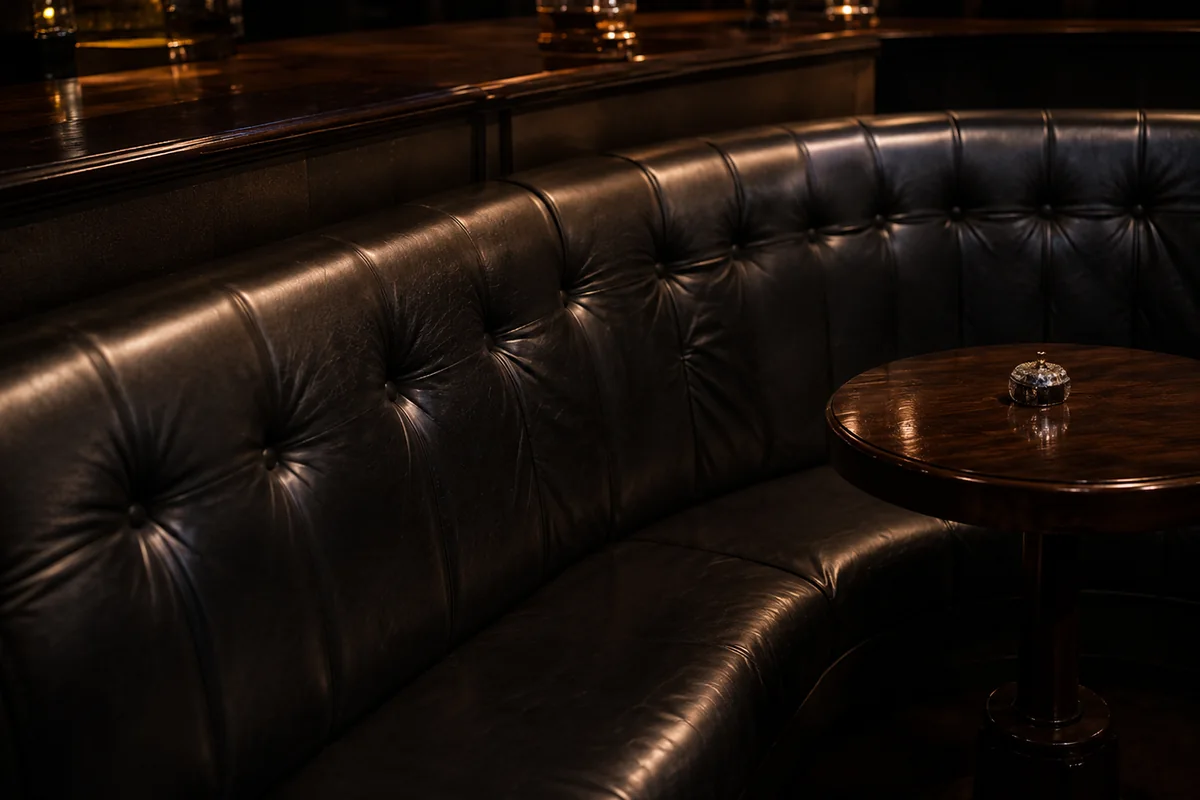 Curved black leather booth beside a polished wood bar and cocktail table