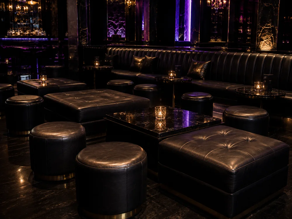 Round and square black leather ottomans around low tables in a nightclub