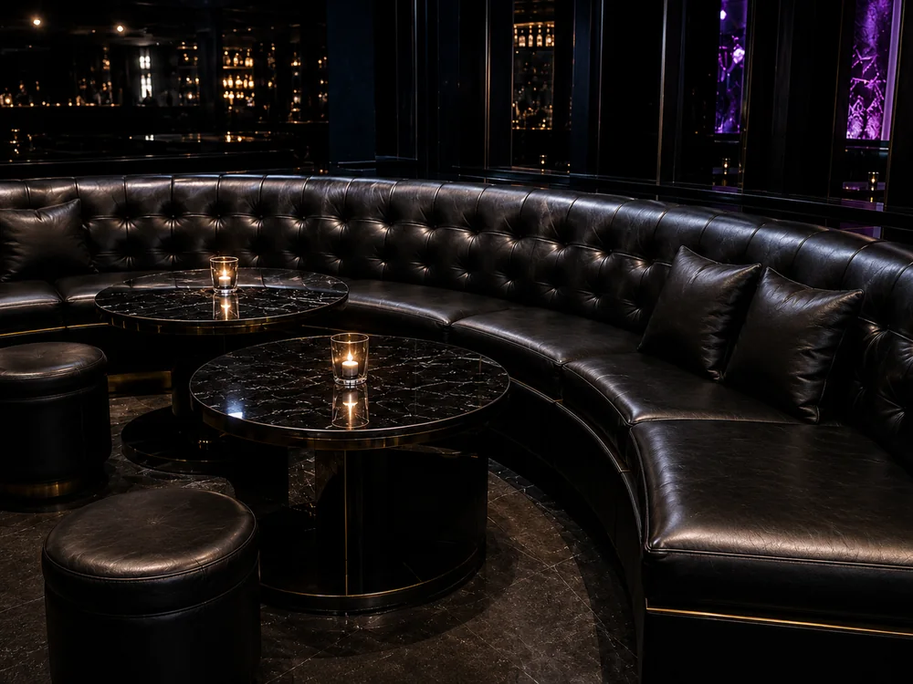 Curved button-tufted black leather VIP booth banquette in a nightclub