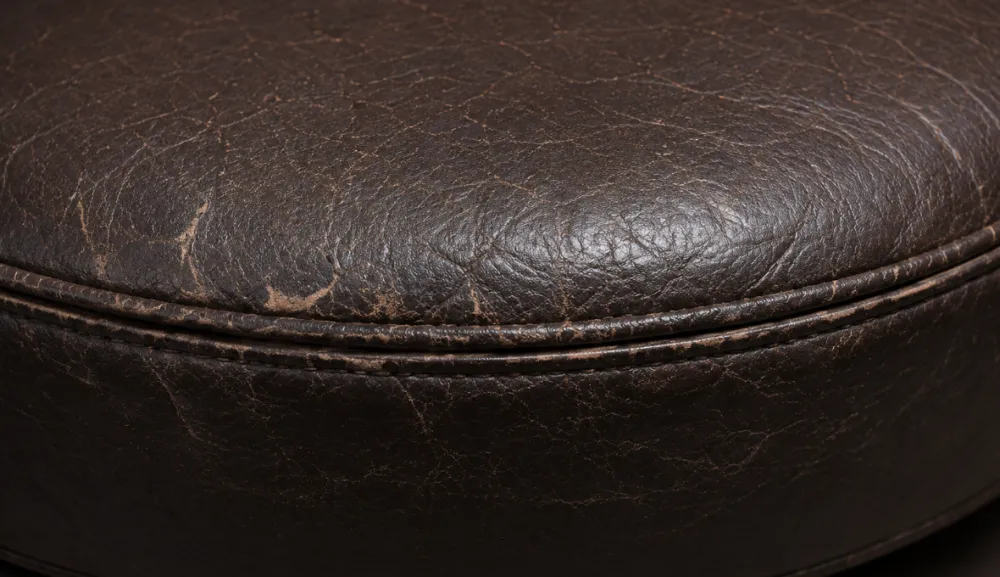Close-up of the rounded front edge of a bonded leather seat cushion with creasing along the piping