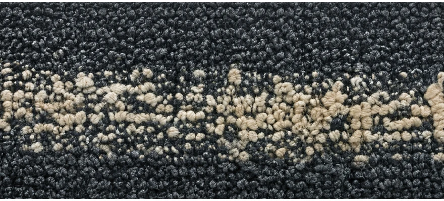 The same charcoal weave worn down: a band of pale undyed yarn core now shows through the surface
