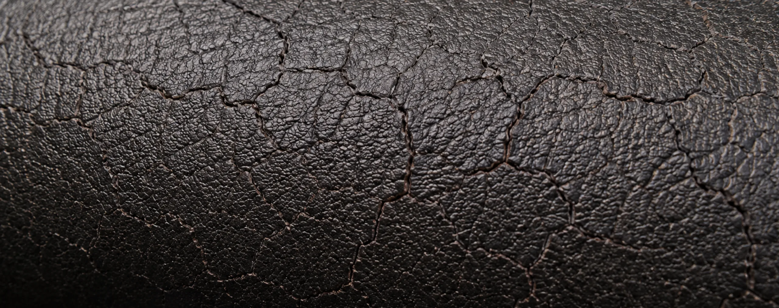 A dense network of fine cracks across hardened dark brown PVC vinyl