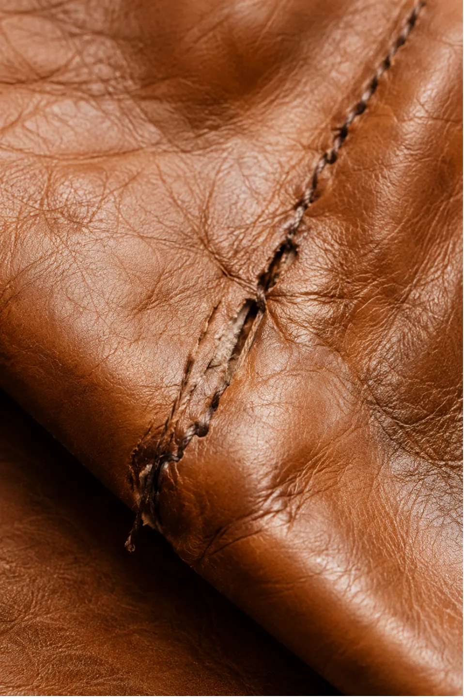 Localized damage on an aniline leather seat panel — a split along the front edge with the surrounding leather still sound