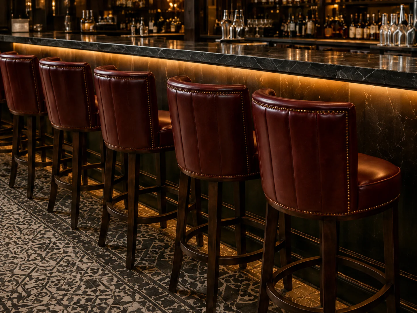 Oxblood leather bar stools along a restaurant counter, seat pads and backs recovered