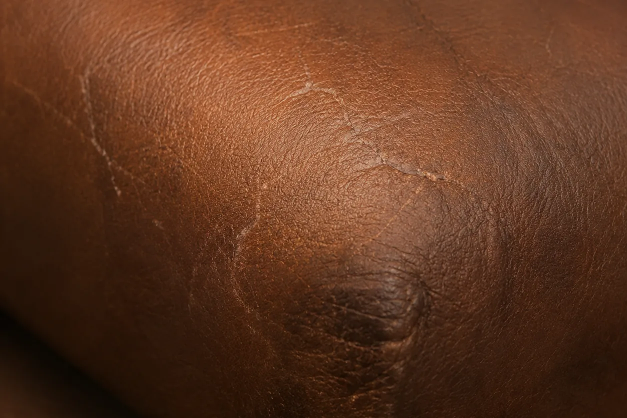 A branching network of fine cracks crazing the finish on a brown leather seat roll