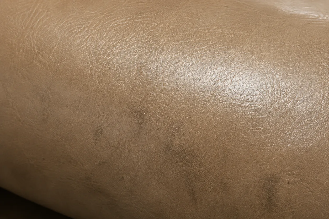 A dark greasy patch soaked into the front roll of a taupe leather restaurant seat