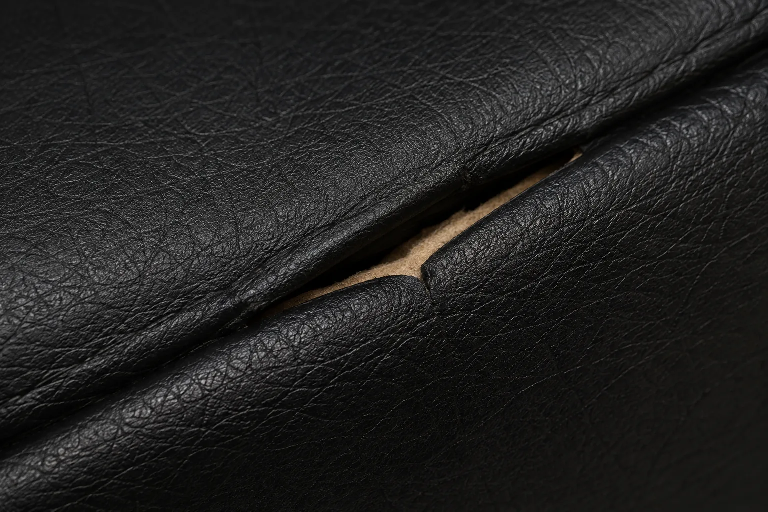 A burst seam on a black leather seat with the tan backing cloth showing through