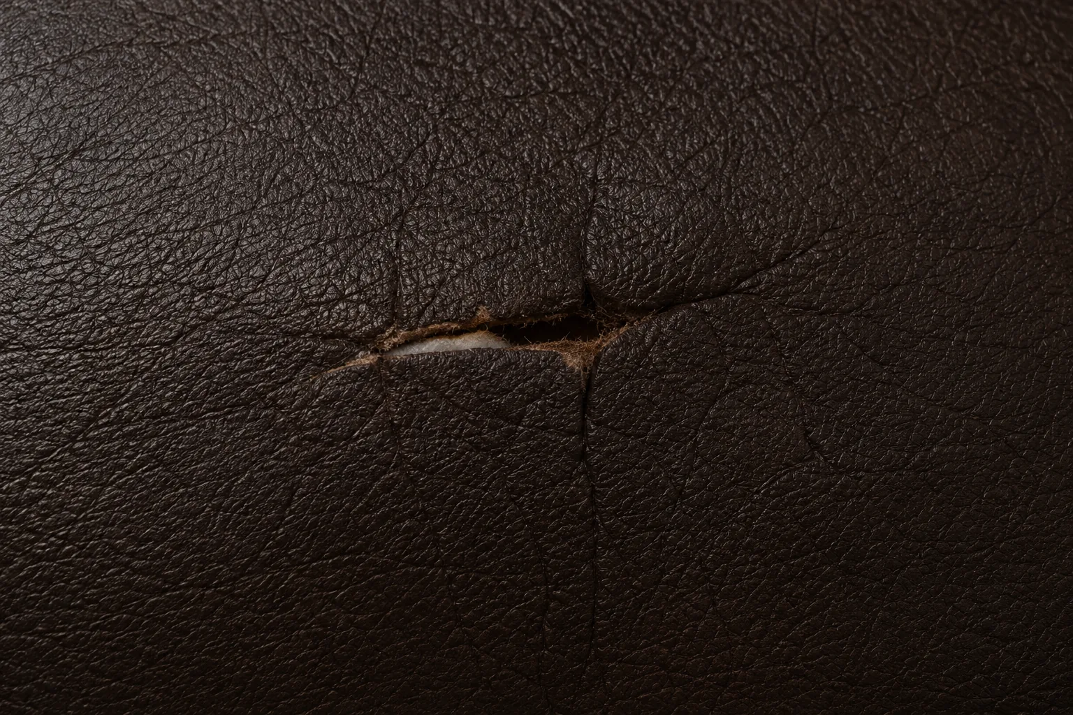Opening in dark brown leather trimmed back to a clean edge beside a seam