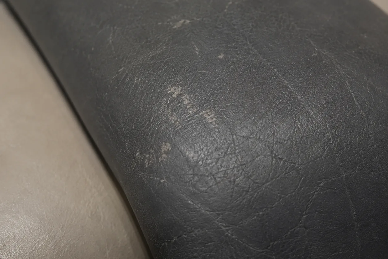 Pale scuffs and surface scratches across a charcoal leather bolster