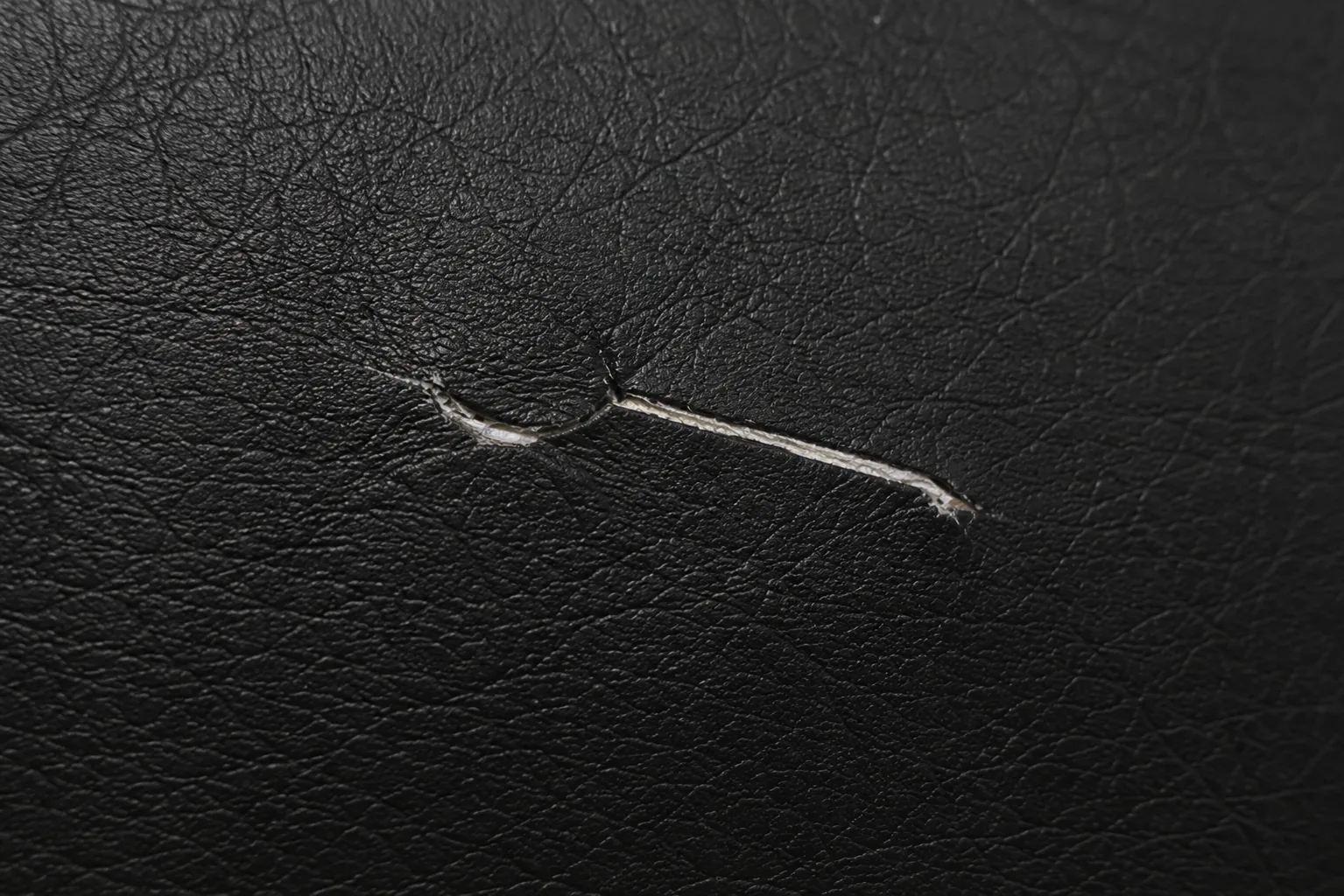 A split in a black vinyl seat where the coating has torn away from its pale backing