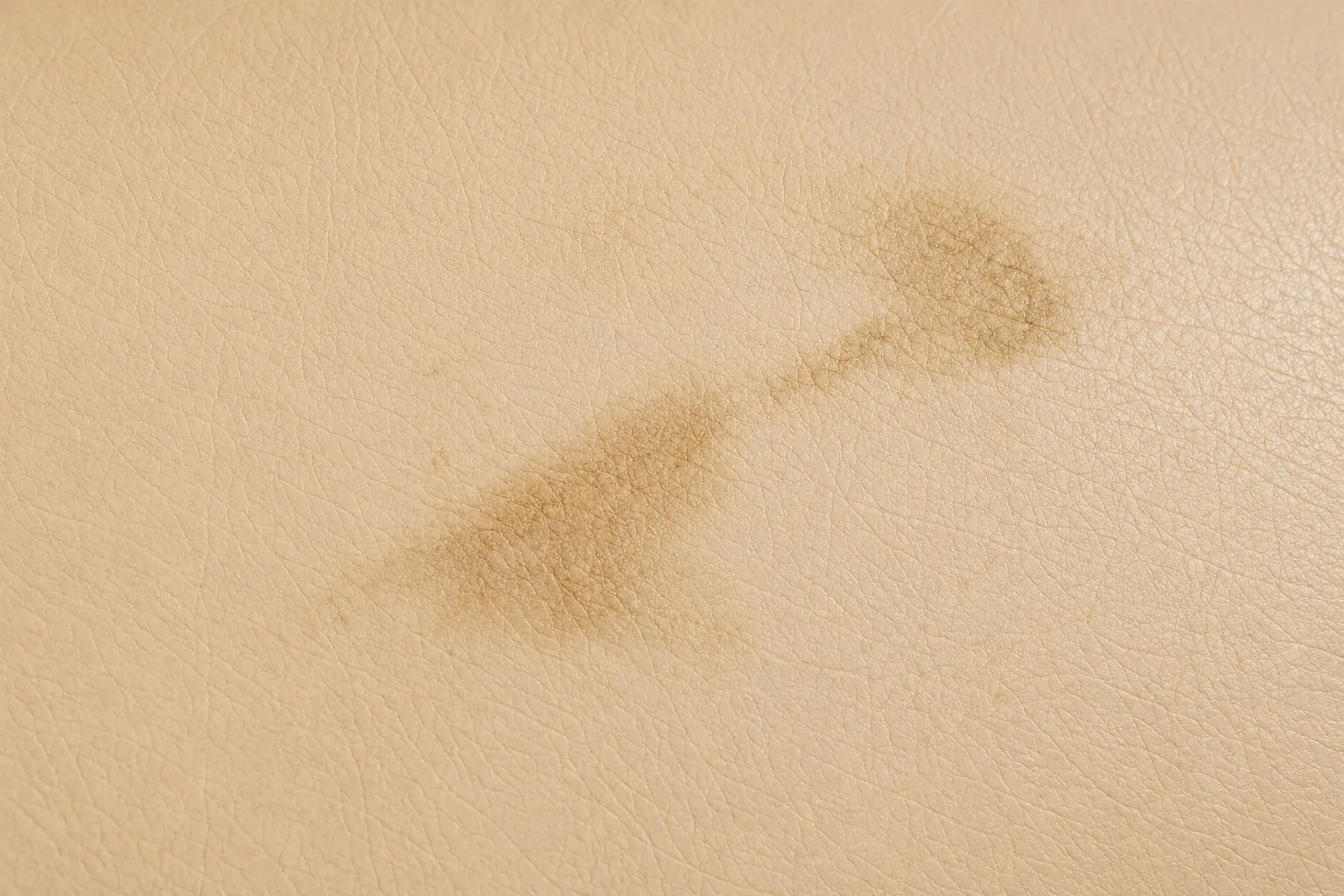 A brown spill stain dried into the surface of a beige leather dining chair seat