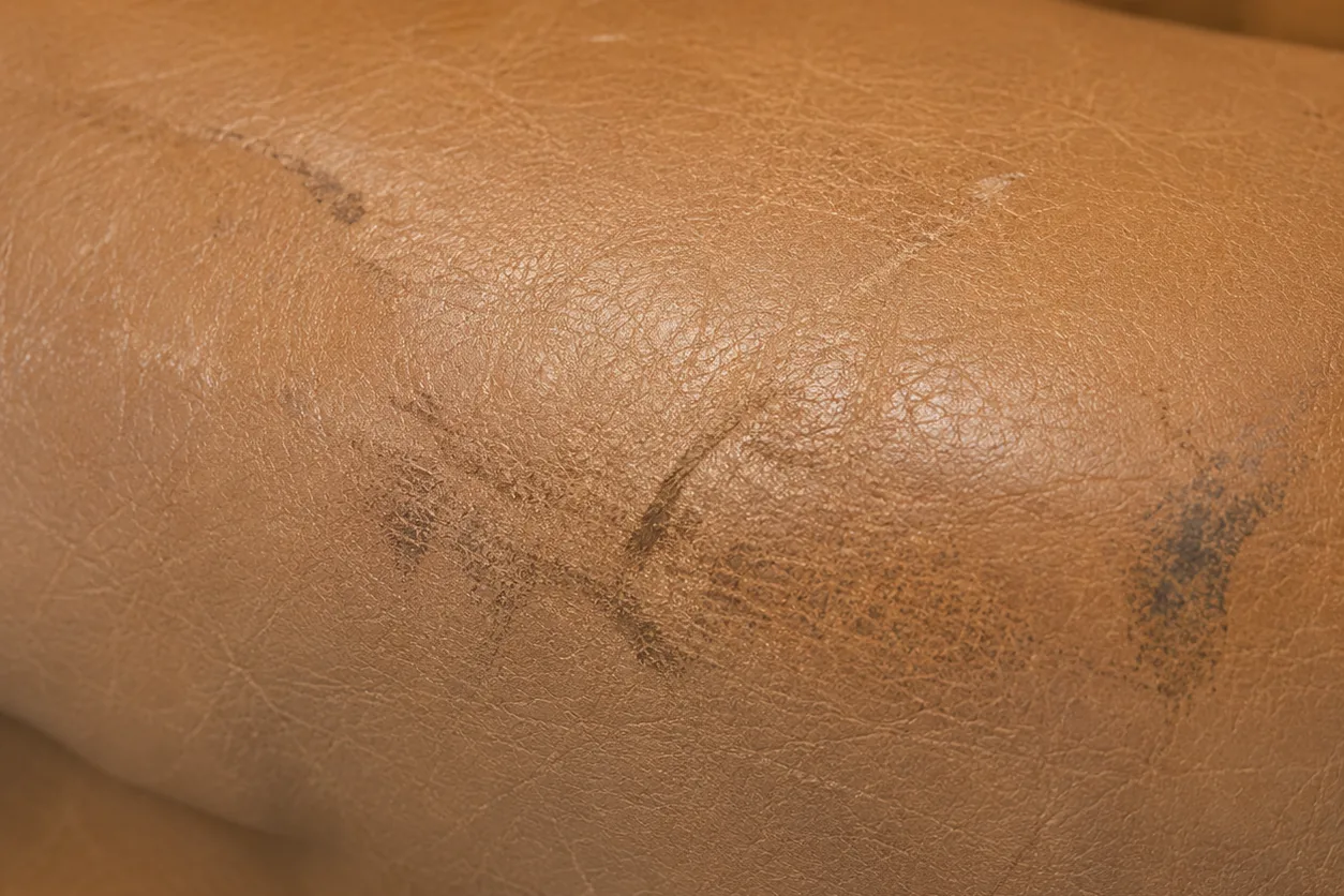 The front edge of a tan leather restaurant seat worn dark and smudged where guests slide across it
