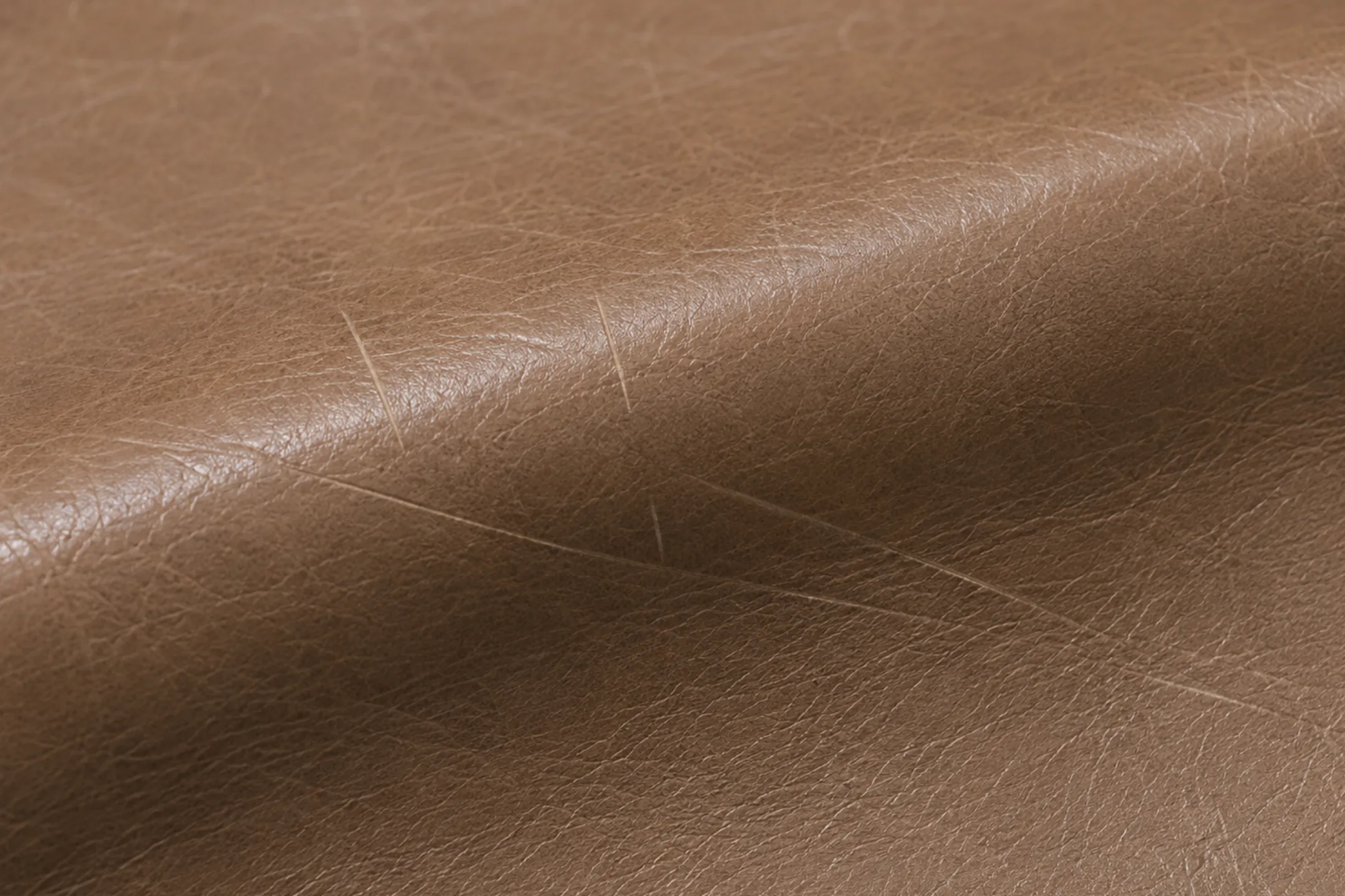 Pale scratch lines scored into the finish of tan semi-aniline leather, reading lighter than the leather around them