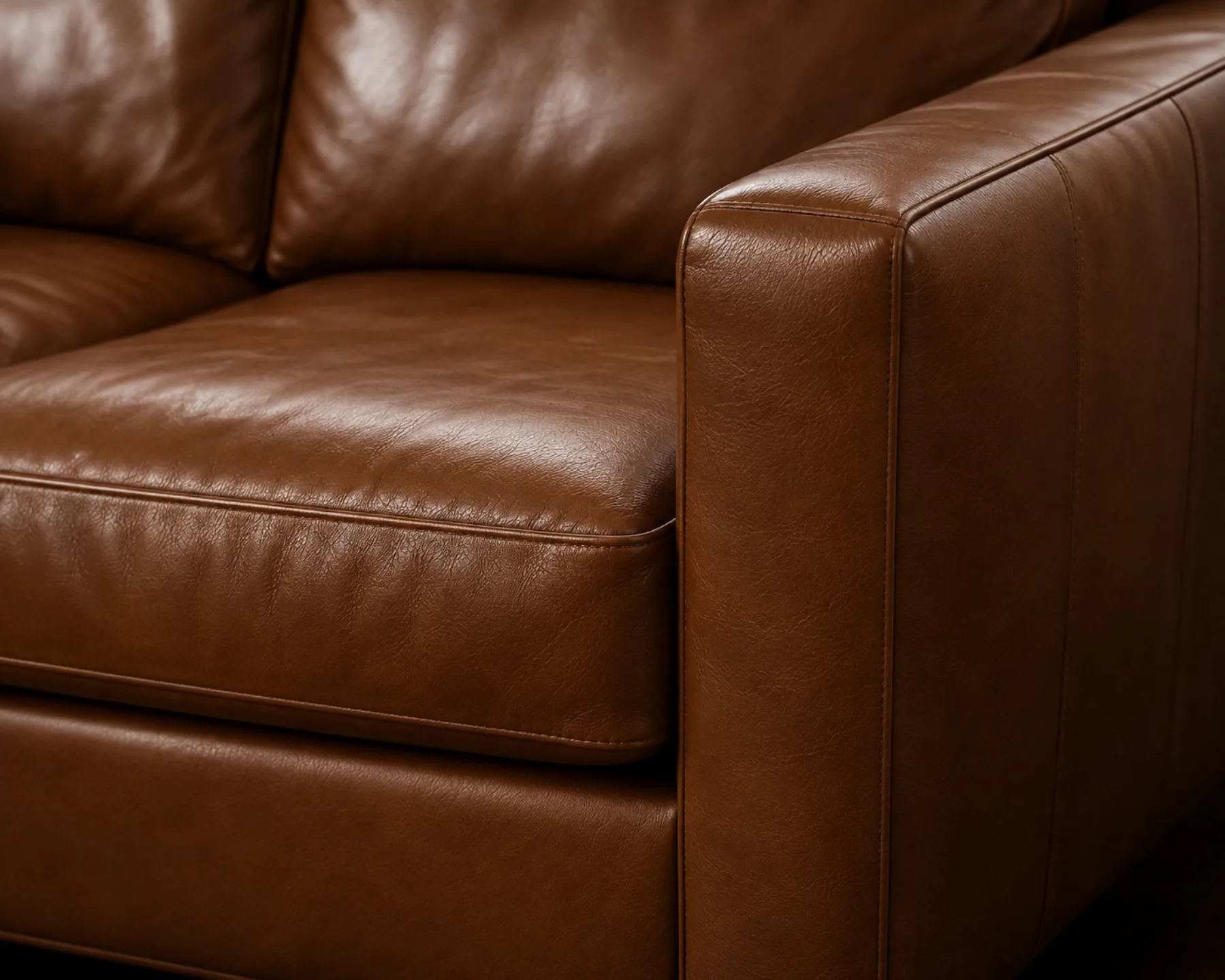 A tan semi-aniline sofa photographed in raking light, the satin highlight continuous across arm and seat