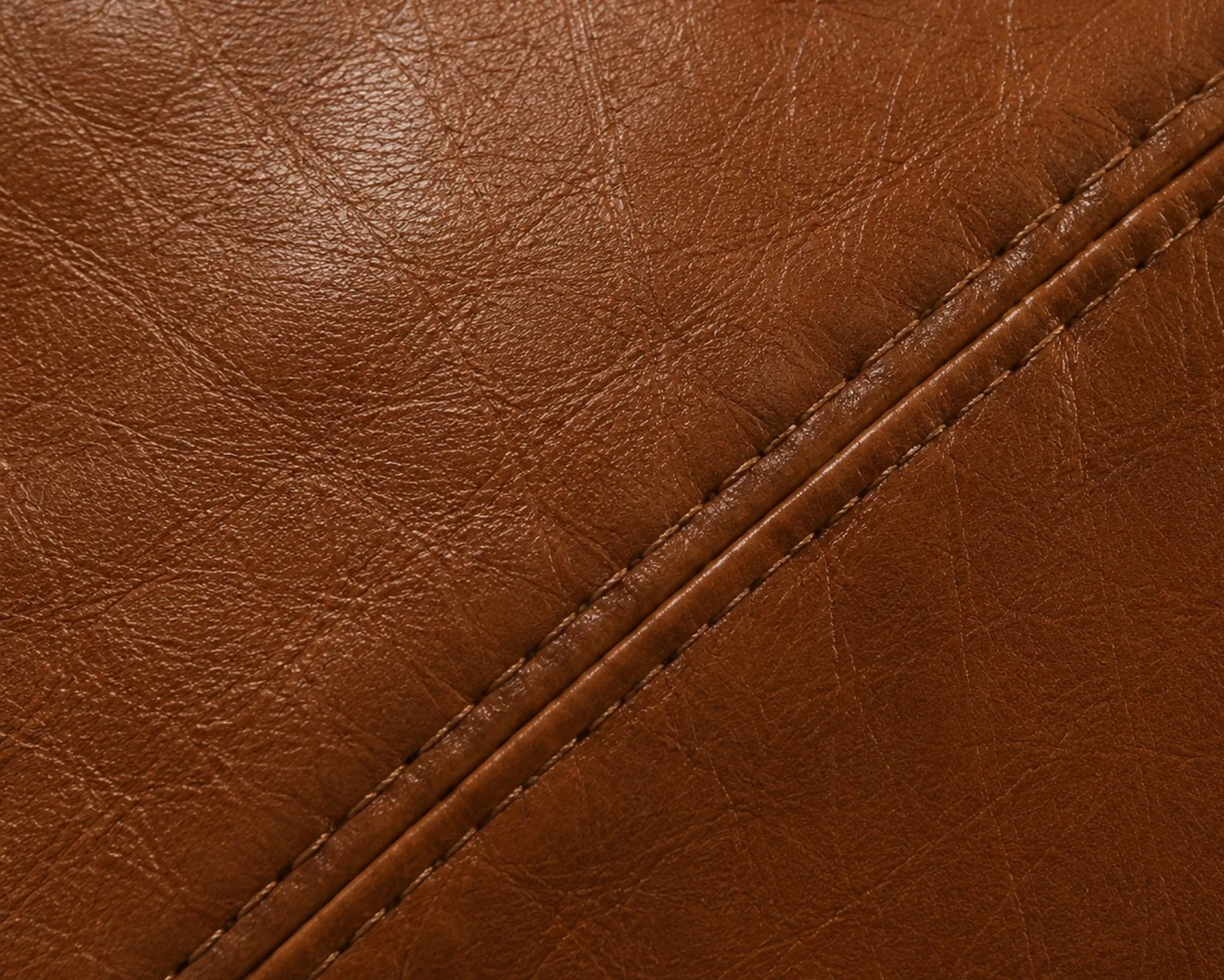 Fine surface scratches across a tan leather cushion interrupting the line of the highlight beside a seam
