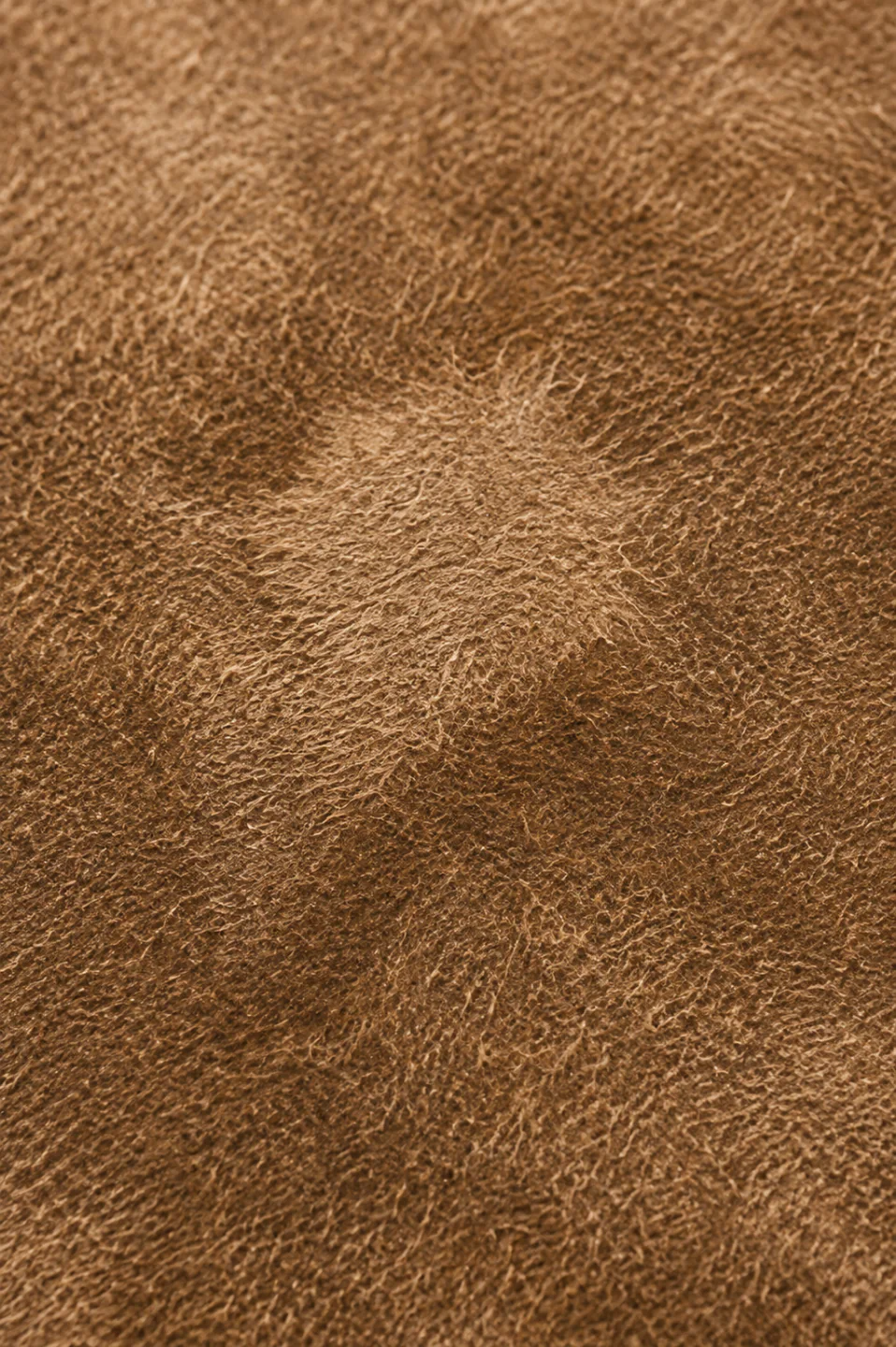 A pale patch on brown suede with a soft undefined edge, where the fibres have been pushed to lie a different way